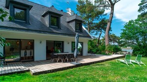 Ein modernes Haus mit einer großen Terrasse, einem Essbereich und Blick auf die umliegende Natur und den See.