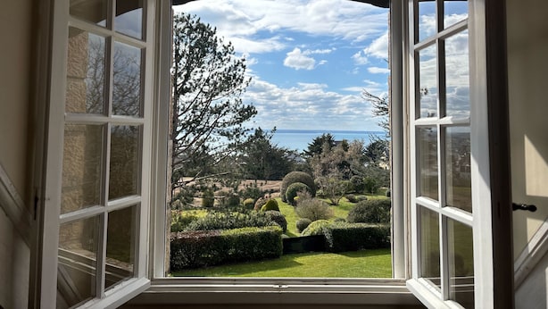 A view through a window with white frames, revealing a well-maintained garden with various shrubs and trees, and a clear sky. - Ker Val - Belle maison avec jardin proche plage (Pléneuf-Val-André)