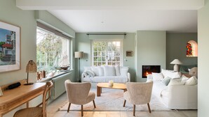 A living room with a white sofa, two armchairs, a coffee table, a fireplace, and a large window with a view of trees. - Ker Val - Belle maison avec jardin proche plage (Pléneuf-Val-André)