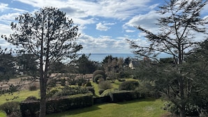 A landscaped garden with a variety of trees and shrubs, a well-maintained lawn, and a distant view of a body of water. - Ker Val - Belle maison avec jardin proche plage (Pléneuf-Val-André)