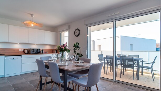 A modern kitchen with white cabinets, a wooden countertop, and a dining area with grey chairs and a table set for four.