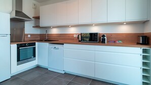 A modern kitchen with white cabinetry, a stainless steel range hood, a microwave, and a dishwasher.