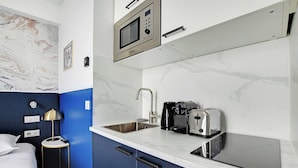 A compact kitchenette with a microwave, toaster, and coffee maker, a sink, and a bedside table with a lamp. - Serene cocoon for 2P with AC - Near Montmartre (Paris)