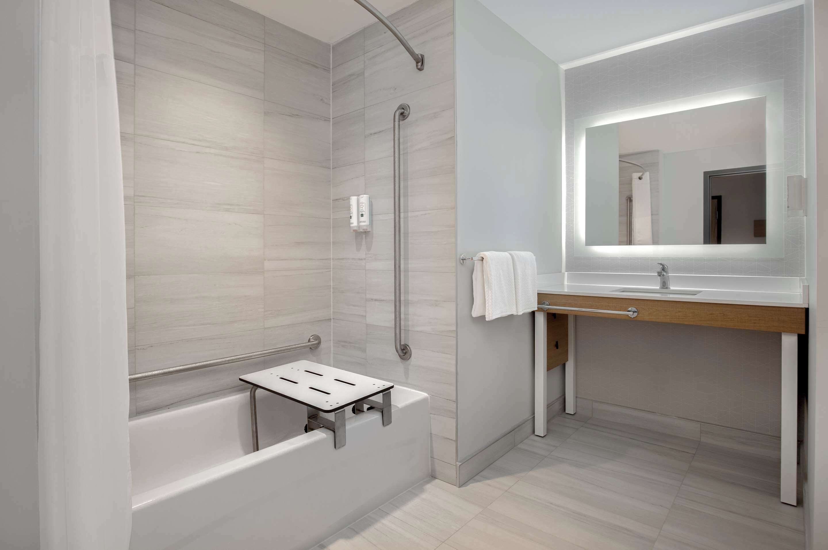 Un baño moderno con ducha a nivel, bañera, tocador con espejo y toallero.