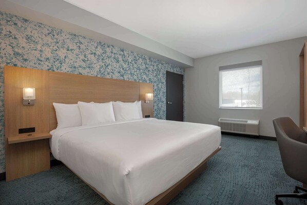 A hotel room with a large bed, two bedside tables with lamps, a window with a view, and a door.