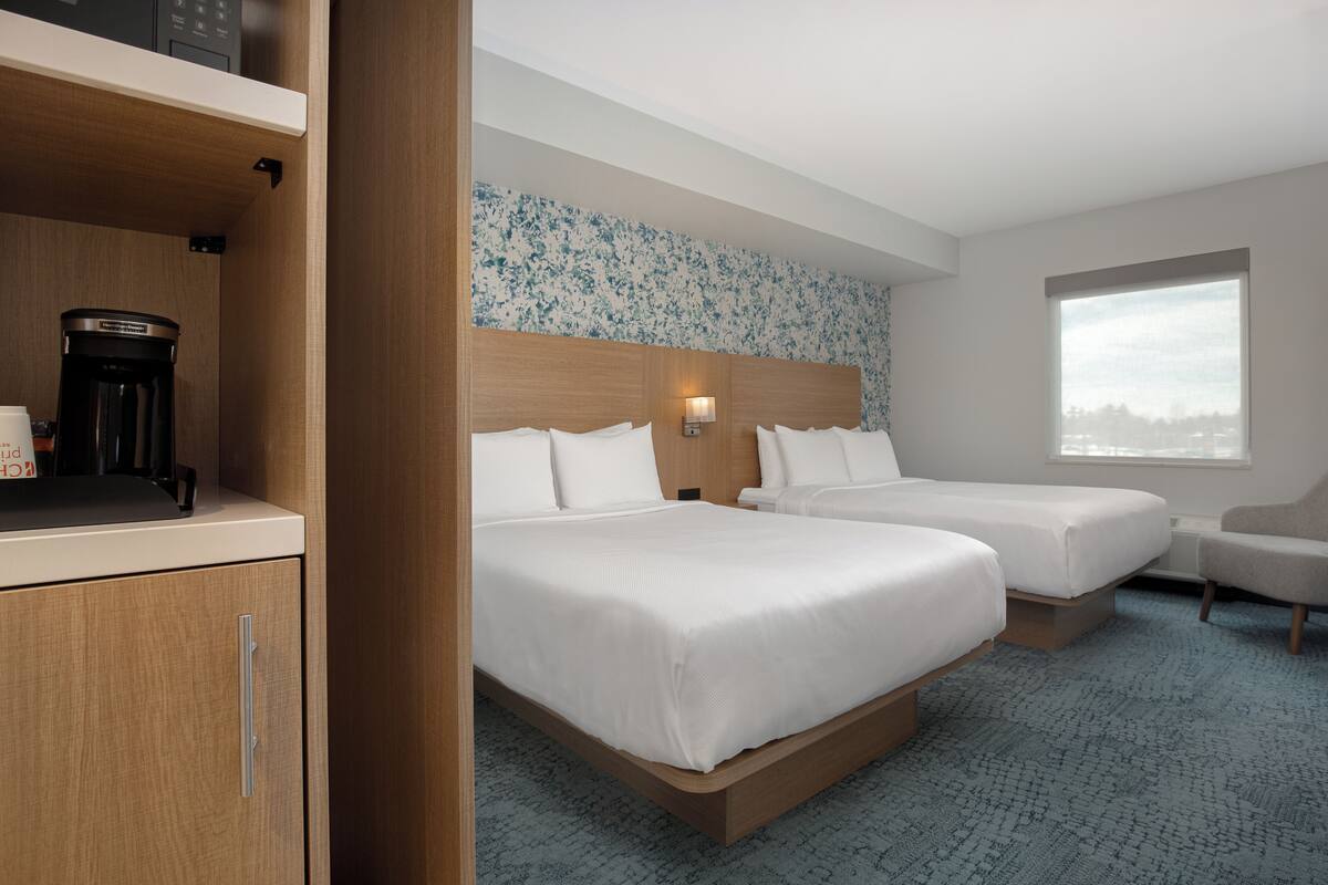 A hotel room with two beds, a coffee maker, a desk, and a window with a city view.