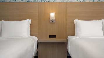 Une chambre d’hôtel avec deux lits, une tête de lit en bois, une table de chevet avec une lampe et un papier peint à motifs floraux.