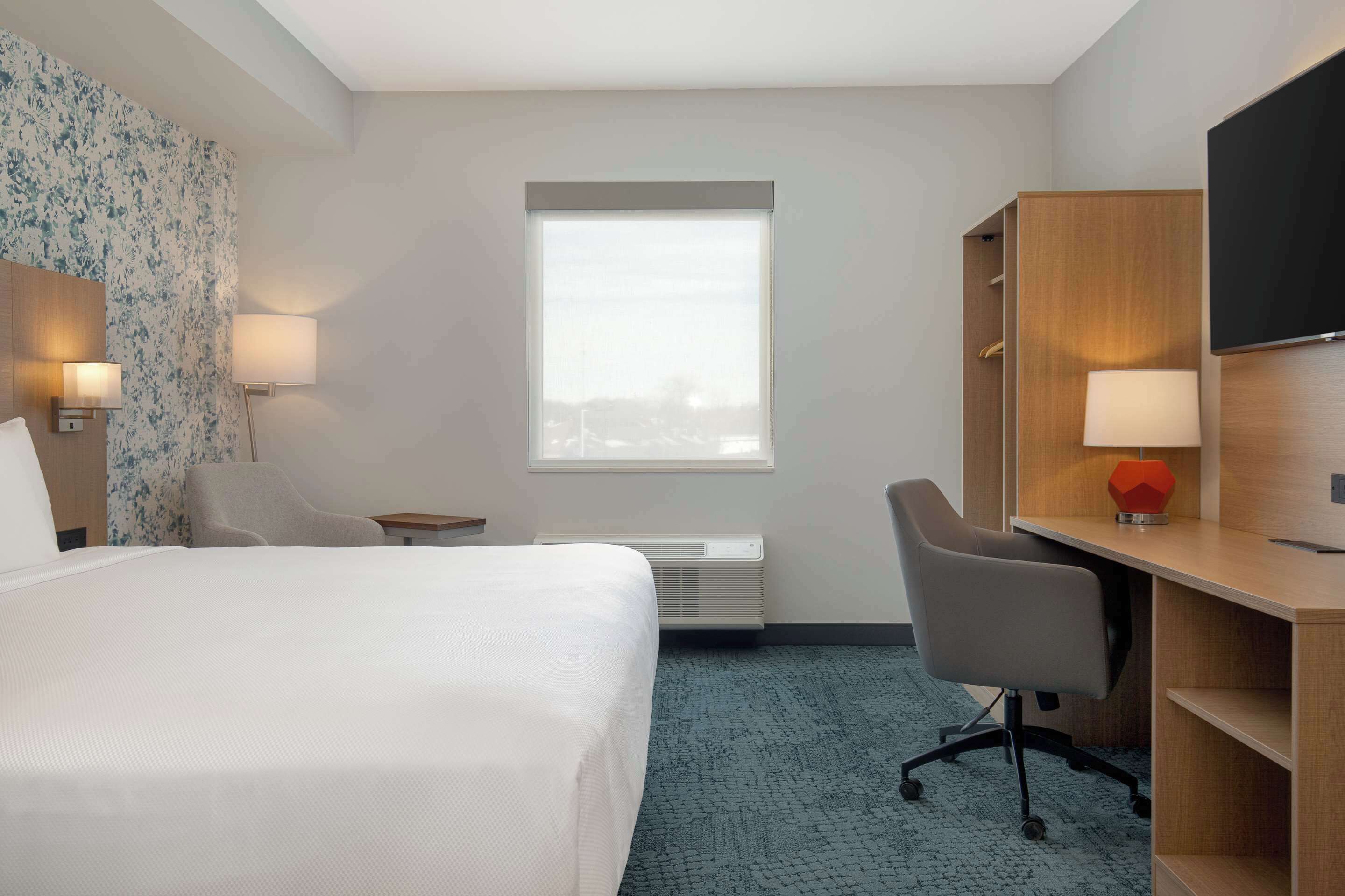 Una habitación de hotel con cama, escritorio, silla, televisión y ventana.
