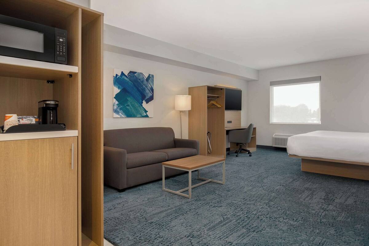 A hotel room with a bed, a sofa, a desk, a coffee machine, a lamp, and a TV.