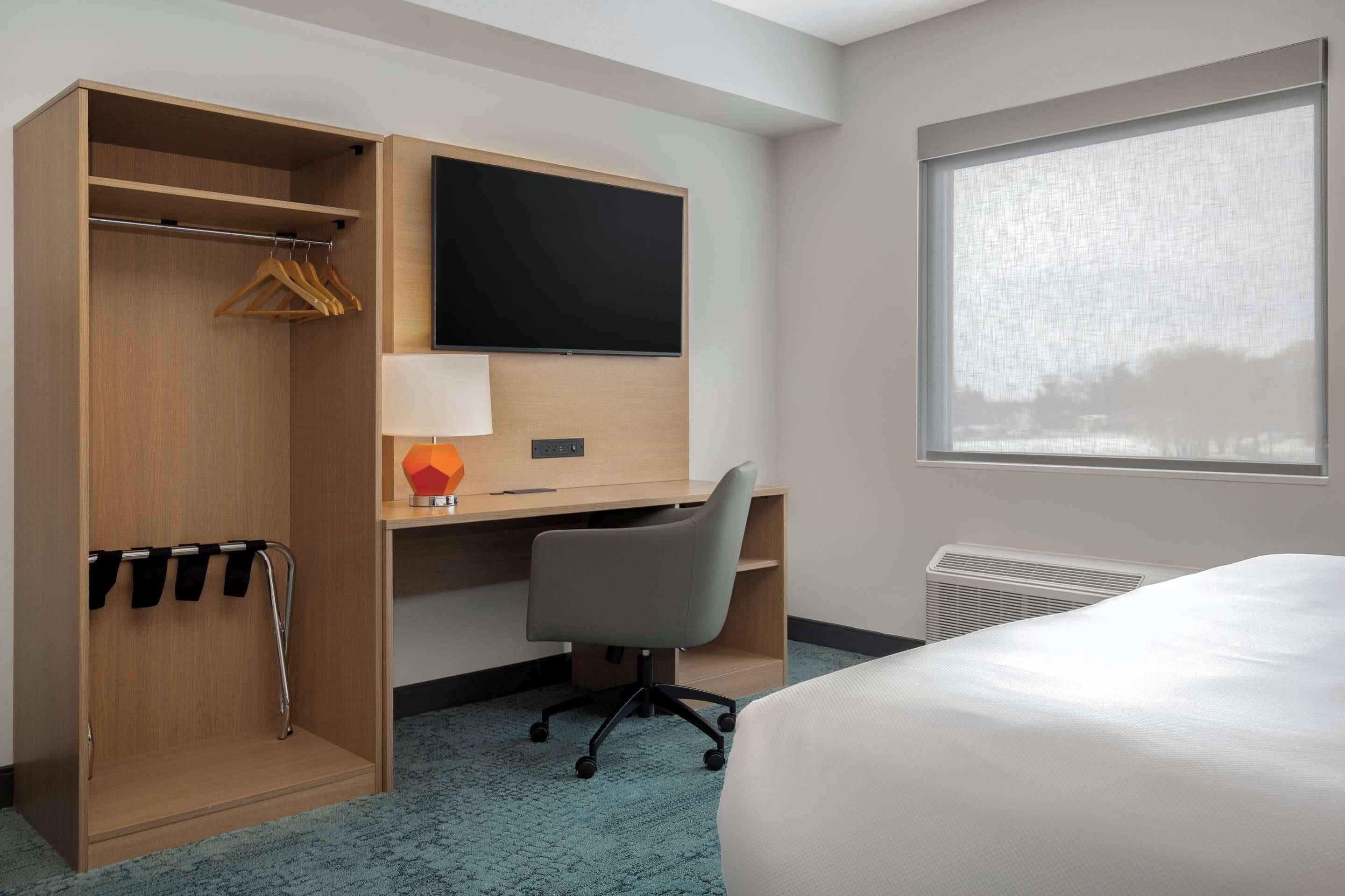 A hotel room with a bed, a desk with a chair, a TV, a wardrobe, and a window with a view.