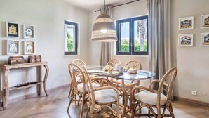 Zona pranzo con sedie in vimini, un tavolo rotondo in vetro e una lampada a sospensione.