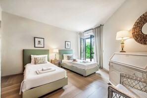 Une chambre d’hôtel avec deux lits, une commode, une lampe et une grande fenêtre avec des rideaux.