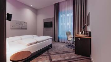 A hotel room with a bed, a desk, a chair, a TV, and a window with curtains.