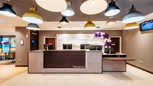 Een hotel receptie met meerdere computerwerkplekken, een houten receptiebalie en een televisie aan de muur.