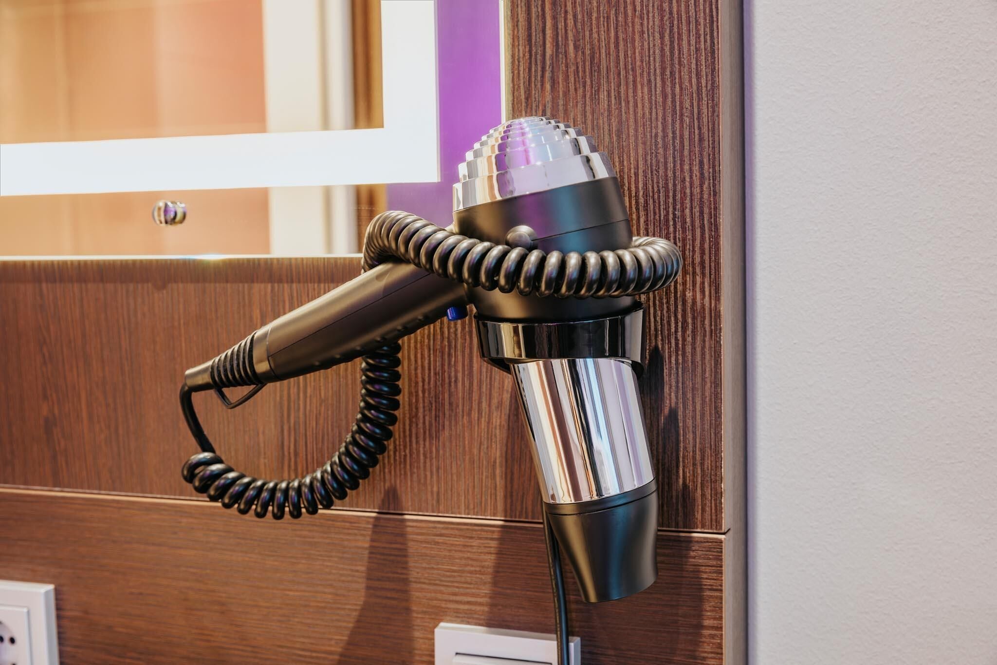 A hairdryer mounted on a wall with a wooden panel background.