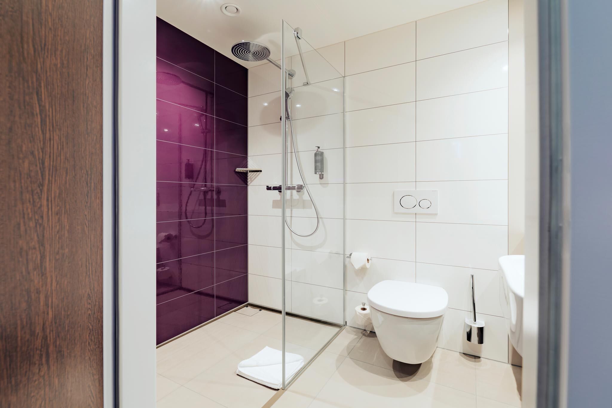 Un baño moderno con cabina de ducha de vidrio, inodoro blanco y pared de acento morada.