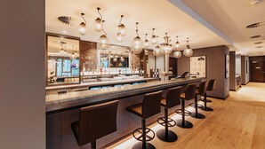 Een bar met meerdere krukken, een toonbank en hanglampen.
