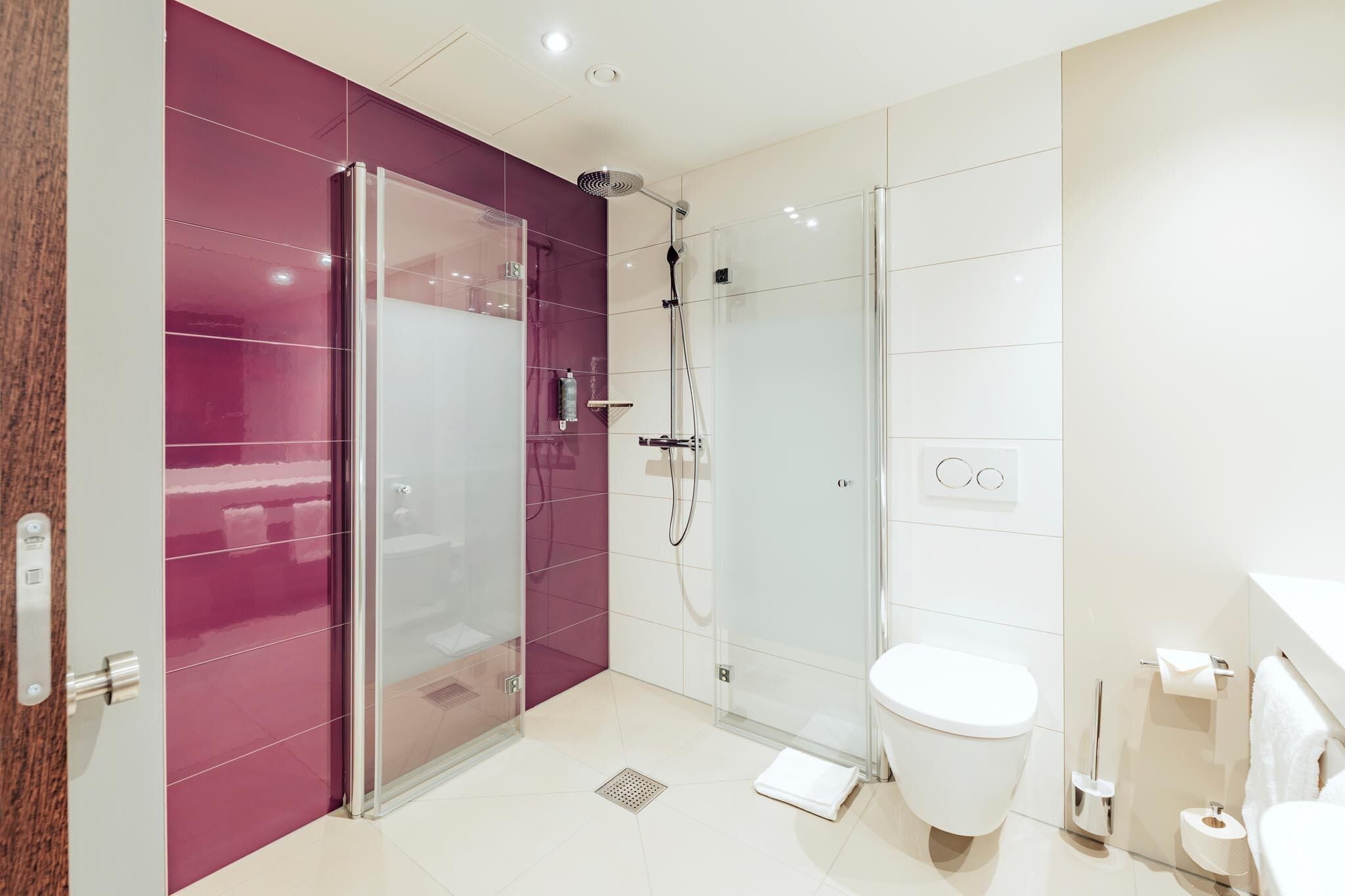 A modern bathroom with a glass shower enclosure, a white toilet, and a marble-tiled floor.