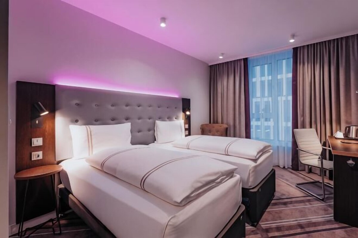Ein Hotelzimmer mit einem großen Bett, einem Schreibtisch, einem Sessel und einem Fenster mit Vorhängen.