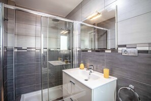 A modern bathroom with a glass-enclosed shower, a white sink with a yellow soap dispenser, and a mirror above the sink. - Villa Bonnie - Three Bedroom Villa, Sleeps 6 (Corralejo)