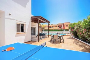 A pool table with a ping pong paddle, a covered seating area, and a pool in a sunny outdoor setting. - Villa Bonnie - Three Bedroom Villa, Sleeps 6 (Corralejo)