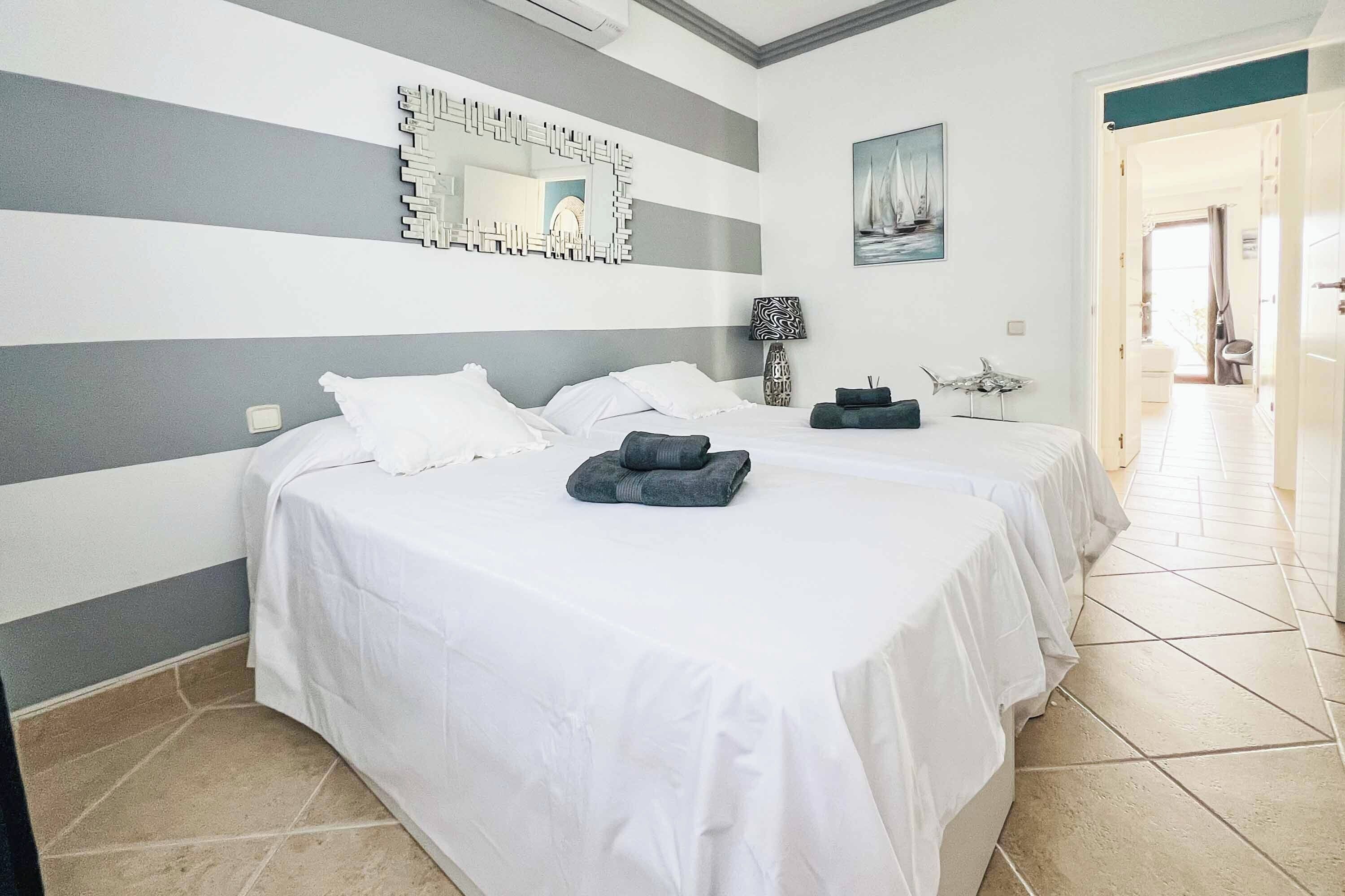 A hotel room with two beds, a large mirror, a painting, and a tiled floor.