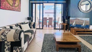 Una sala de estar con un sofá, una mesa de centro, televisor y vistas al exterior a través de un ventanal.
