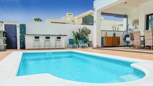 Una piscina con cubierta blanca, dos sillas reclinables, un comedor y una planta decorativa.