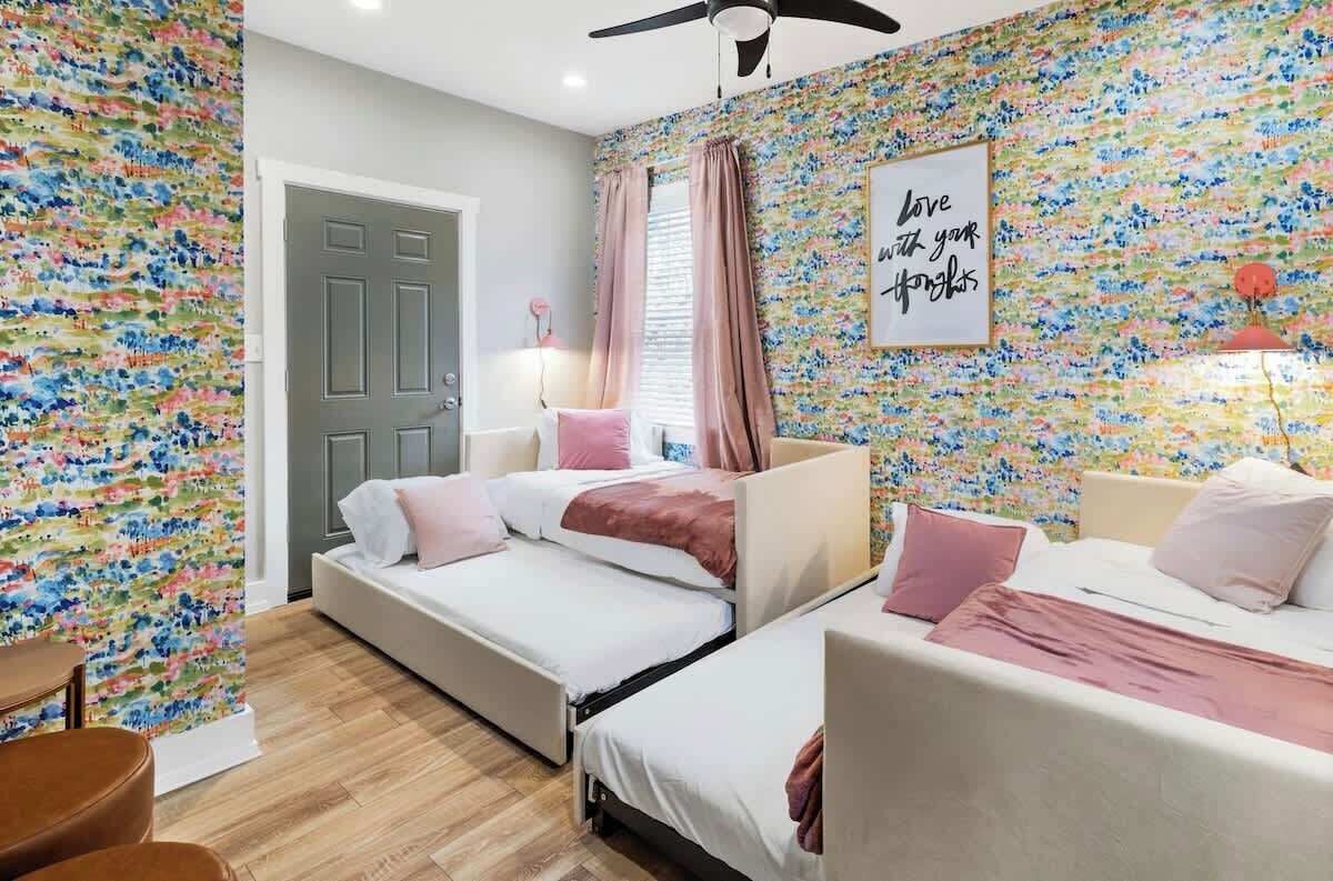 A bedroom with two beds, a door, a ceiling fan, and a floral wallpaper.