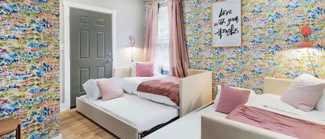 A bedroom with two beds, a door, a ceiling fan, and a floral wallpaper.