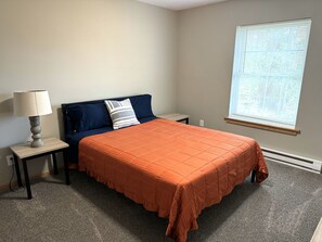 A bedroom with a bed, a nightstand, a lamp, a window, and a wall socket. - Rusty Rim Bike House Unit 1, Centrally located, 2 bed 1 bath (Crosby)