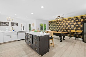 A modern kitchen with a central island, a dining area with a pool table, and a living space with a patterned wall. - Casita Delray Oasis: 4BR with Pool, Hot Tub, BBQ, Firepit, Pool Table (Delray Beach)