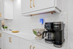 Una cocina moderna con armarios blancos, una cafetera Keurig y una cesta decorativa.