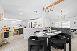 A modern kitchen with white cabinets, a central island, and a dining area with a black table and chairs. - Casita Delray Oasis: 4BR with Pool, Hot Tub, BBQ, Firepit, Pool Table (Delray Beach)