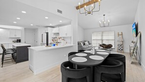 A modern kitchen with white cabinetry, a central island, and a dining area with a black table and chairs.
