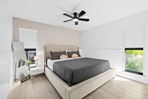 Un dormitorio moderno con cama, mesitas de noche, ventilador de techo y ventana con vistas.