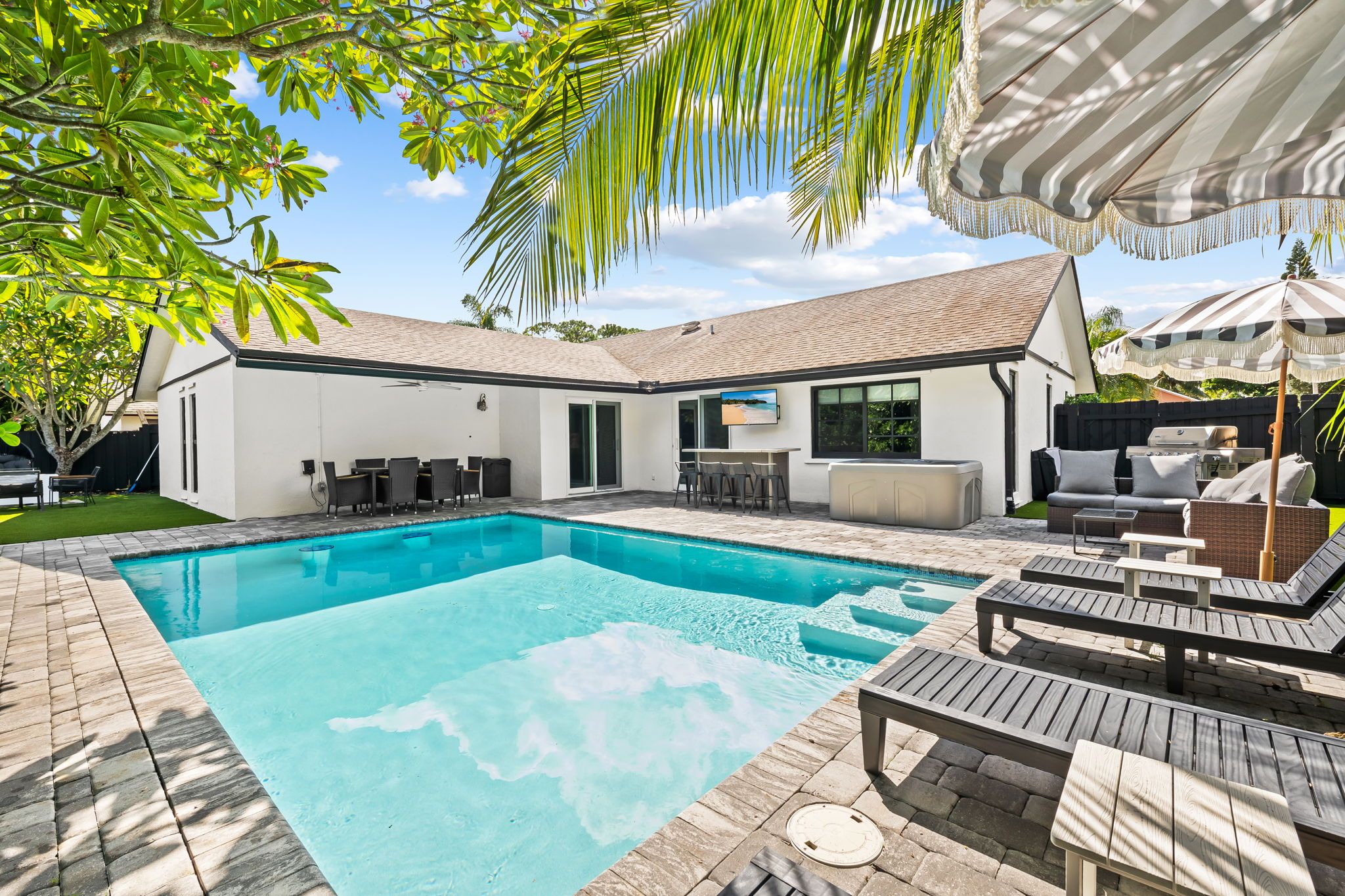 A modern house with a swimming pool, outdoor seating, and a TV screen.
