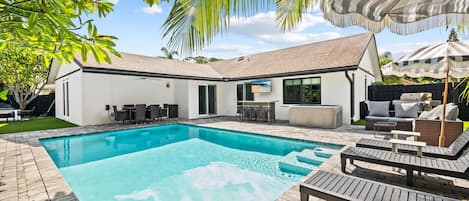 A modern house with a swimming pool, outdoor seating, and a TV screen.