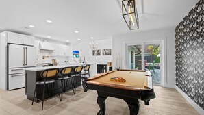 A modern kitchen with white cabinets, a central island, and a pool table.