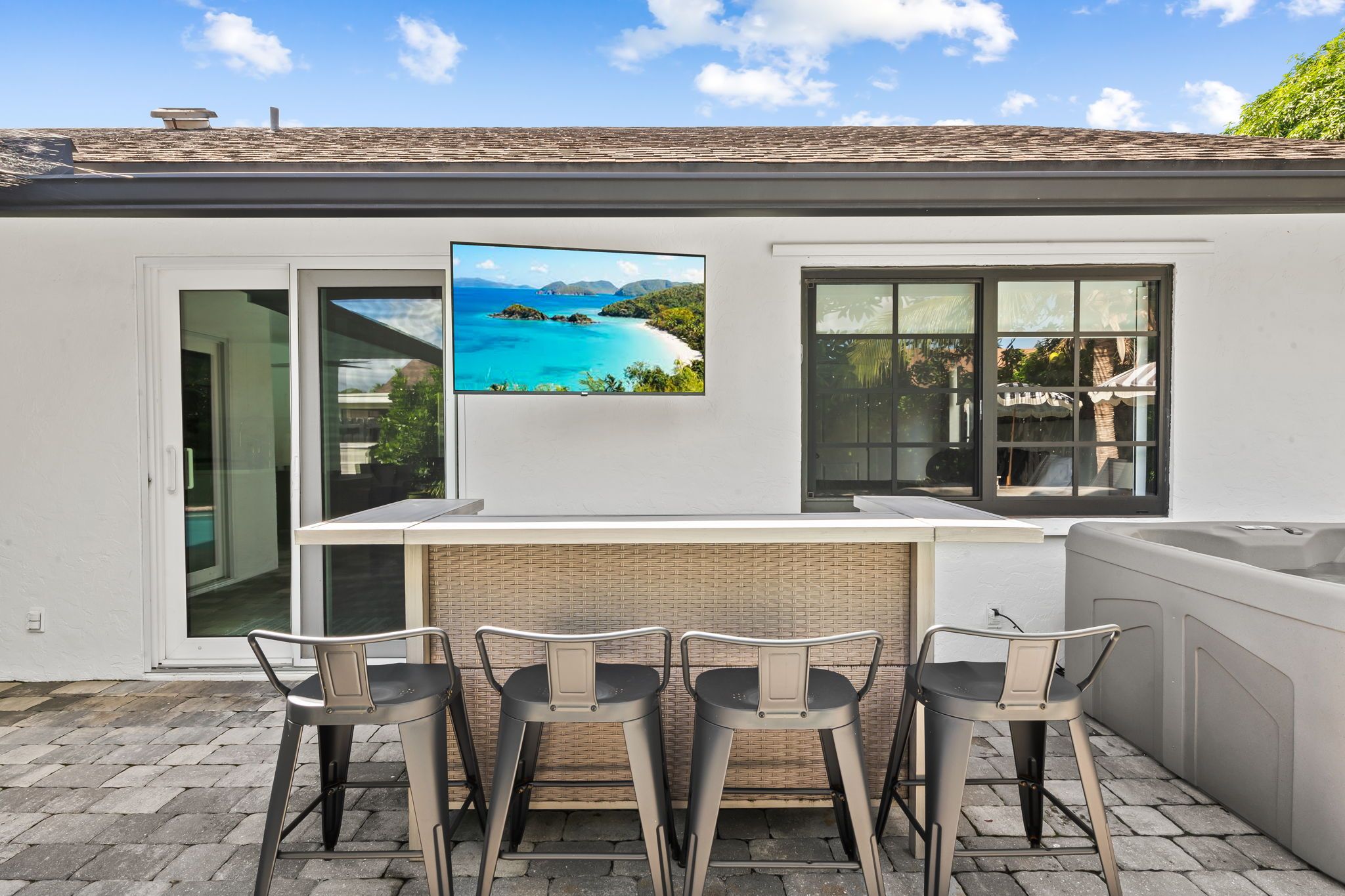 An outdoor bar area with a view of a tropical beach, a glass door leading to a patio, and a brick wall.