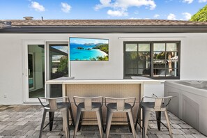 Eine Außenbar mit Blick auf einen tropischen Strand, eine Glastür, die auf eine Terrasse führt, und eine Backsteinmauer.