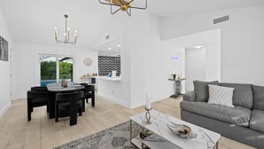 A modern living room with a grey sofa, a dining table with chairs, and a chandelier.