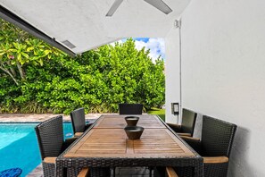 An outdoor dining area with a pool, surrounded by lush greenery. - Casita Delray Oasis: 4BR with Pool, Hot Tub, BBQ, Firepit, Pool Table (Delray Beach)