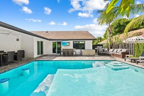 A backyard with a swimming pool, outdoor seating, and a TV screen.
