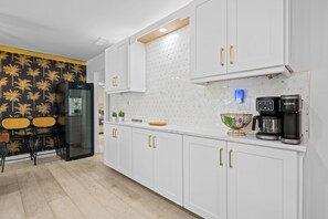 A modern kitchen with white cabinets, a black refrigerator, a coffee maker, and a patterned wall. - Casita Delray Oasis: 4BR with Pool, Hot Tub, BBQ, Firepit, Pool Table (Delray Beach)