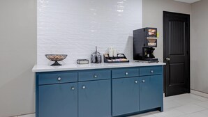 Una cocina con un mueble azul, una encimera blanca, una cafetera y una puerta.