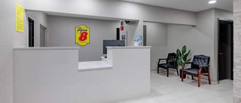 A reception area with a reception desk, chairs, a plant, and a sign indicating a Super 8 hotel.