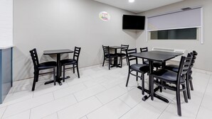 Un comedor con mesas y sillas, un televisor de pantalla plana montado en la pared, y un logotipo en la pared.