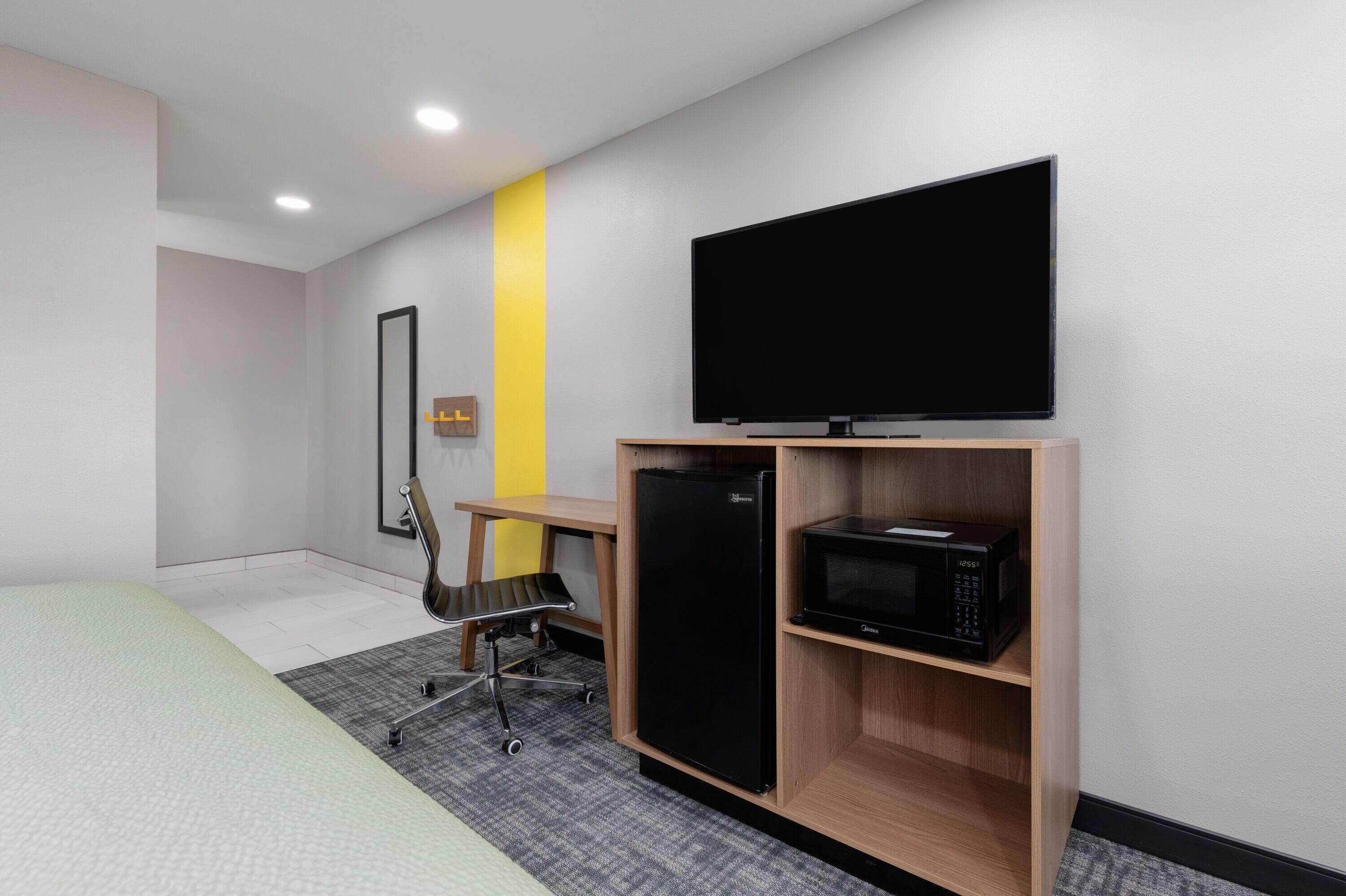 Habitación de hotel con cama, escritorio con silla, televisor de pantalla plana, refrigerador y microondas.