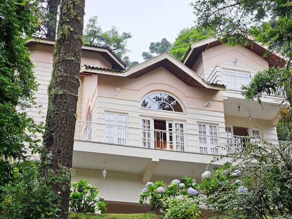 Stunning building with a central arched window and balcony, set amidst lush greenery.